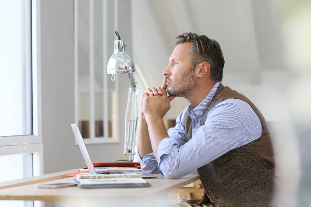Man in office looking through window, being thoughtful