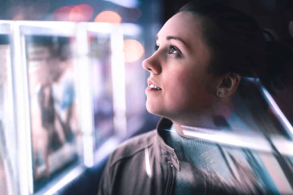 Serious thoughtful woman looking at city lights at night in dark. Dramatic face with reflection of billboard signs. Pensive lady thinking. Side view.