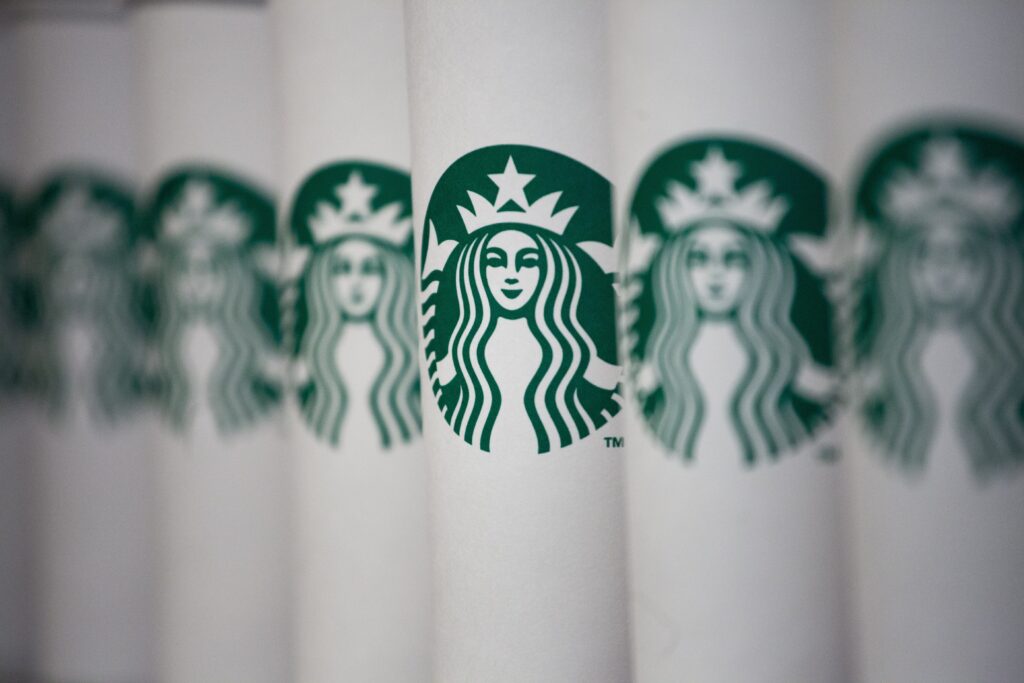 A close-up image of multiple paper cups lined up, each featuring the green Starbucks logo with the iconic mermaid, subtly showcases marketing psychology. The cups are slightly angled, creating a repetitive pattern that taps into consumer behavior.