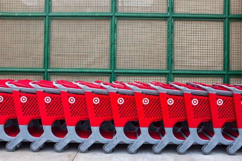 A row of red shopping carts lined up neatly in front of a large green wire mesh wall. The carts have a distinct pattern and logo, and are parked side by side on a concrete surface.