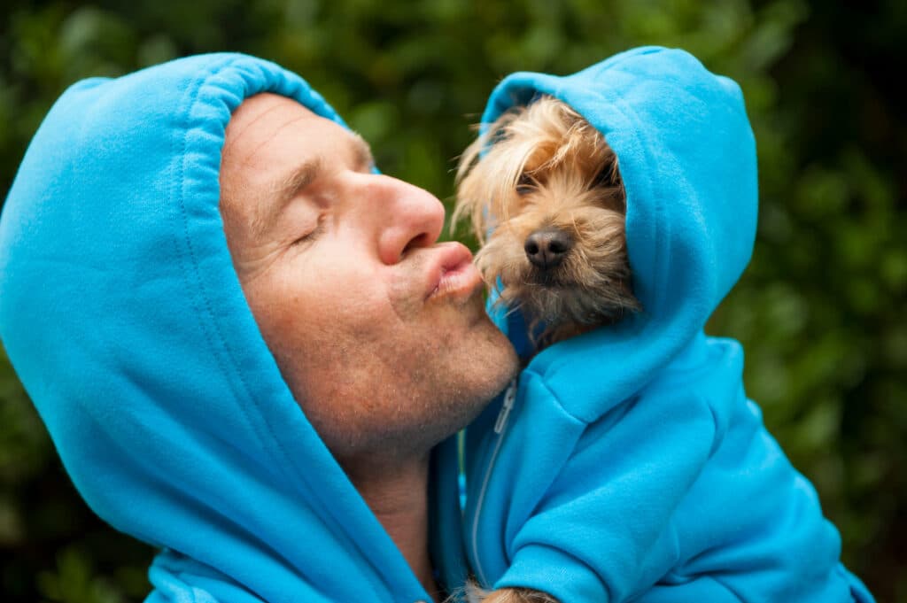 Portrait of dog owner kissing a furry friend in matching blue ho