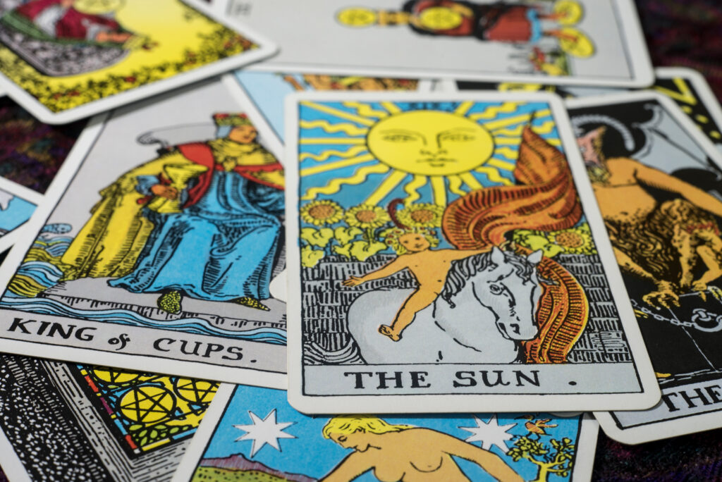 A close-up photo of various tarot cards scattered on a surface. The prominent card, "The Sun," shines brightly, drawing parallels to marketing psychology in its ability to captivate. Other visible cards include "King of Cups" and colorful, intriguing illustrations that echo elements of behavioral economics.