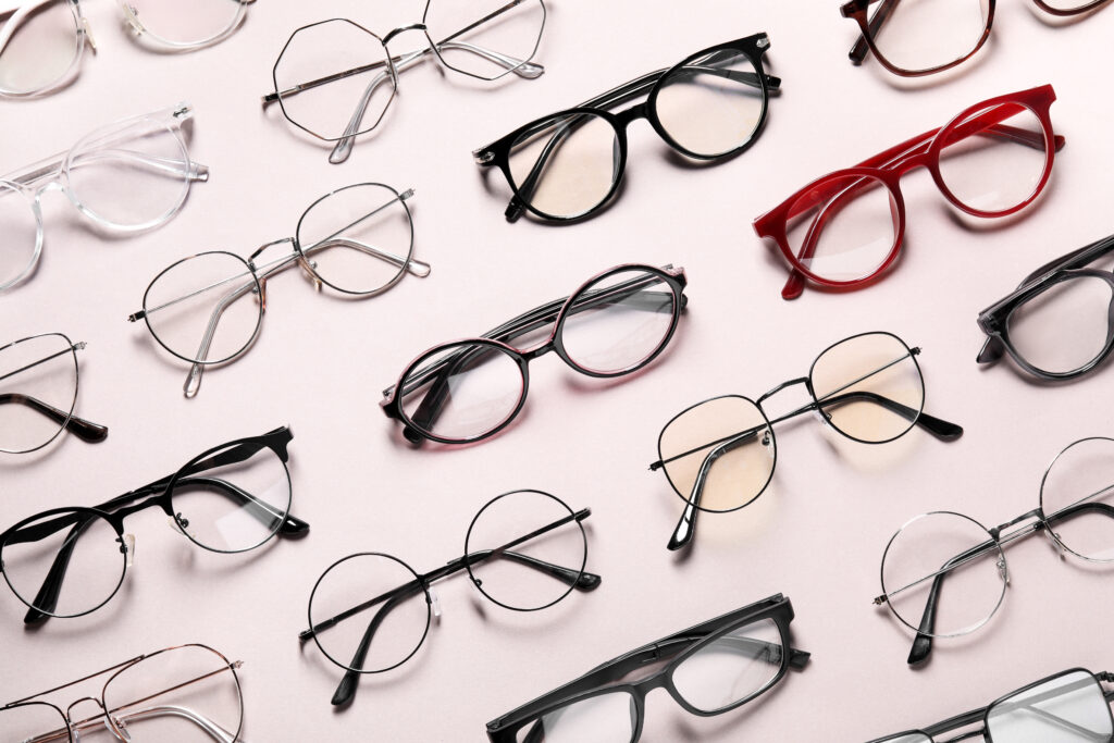 A collection of eyeglasses in various styles and colors, including black, red, and clear frames, are arranged on a light pink background. Designed with marketing psychology in mind, these glasses feature diverse shapes like round, oval, and angular to appeal to varied consumer behavior.