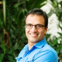 Smiling man wearing glasses and a blue shirt, exuding confidence in front of lush green foliage—a perfect embodiment of marketing psychology in action.